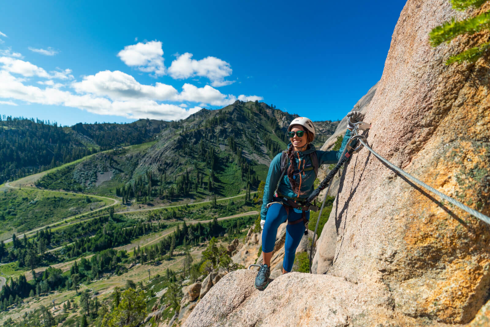 A female climber on the Tahoe Via Ferrata overlooking Palisades Tahoe and Olympic Valley, CA. One of the best Lake Tahoe adventures!
