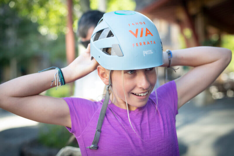 A young girl fastens her helmet to climb the Tahoe Via Ferrata at Palisades Tahoe in Olympic Valley. One of the best Lake Tahoe adventures!